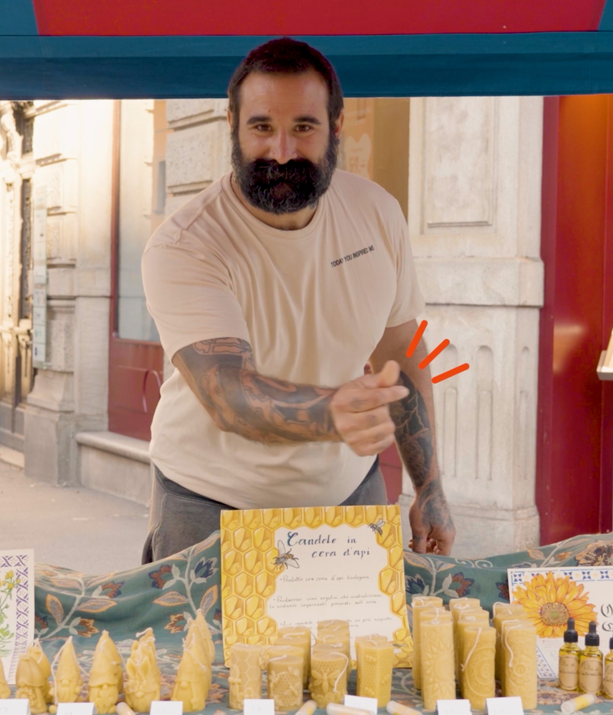 Artigiano con la barba mostra le sue candele in cera d'api fatte a mano durante un mercato locale in Ticino. Esempio di eccellenza nell'apicoltura e nell'artigianato ticinese.